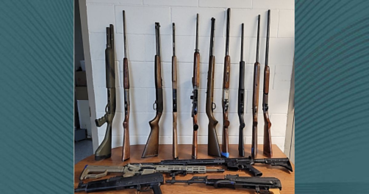 Una variedad de armas apoyadas contra una pared y sobre una mesa incautadas por oficiales de CBP en el puerto de entrada de Eagle Pass durante un examen de salida.